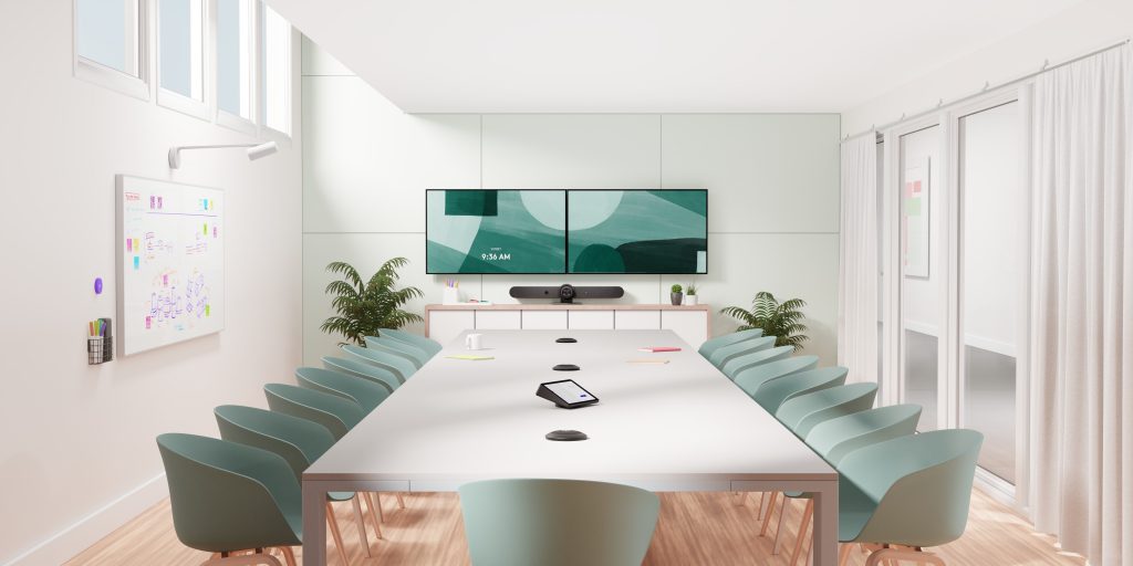 Sala de reuniones grande con mesa larga, doble pantalla y micrófonos de mesa